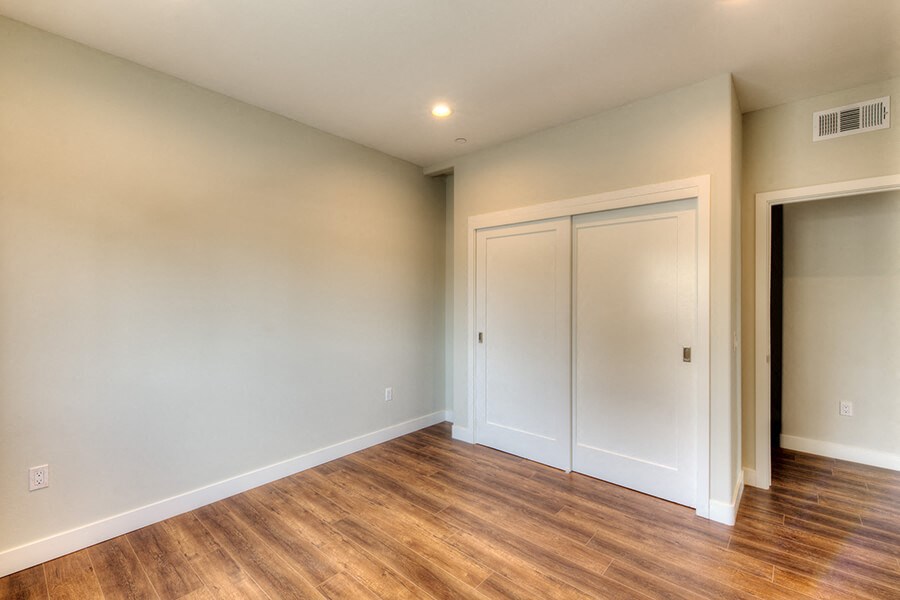 a room with white walls and wood flooring and two closets