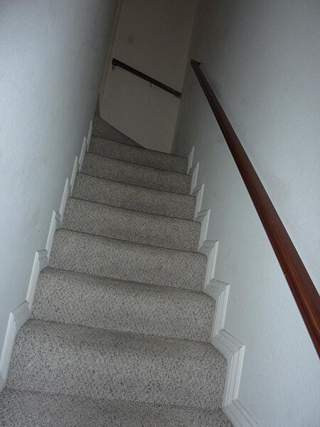 a carpeted staircase with a wooden railing and a white wall