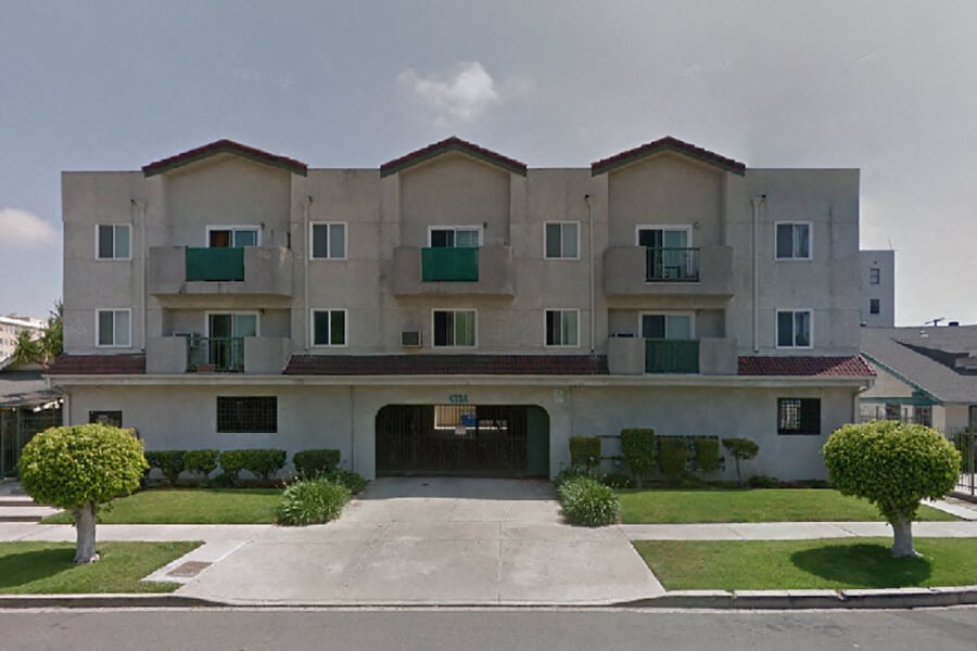 a white apartment building with green balconies and a driveway