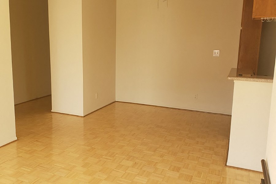an empty living room with wood flooring and a kitchen