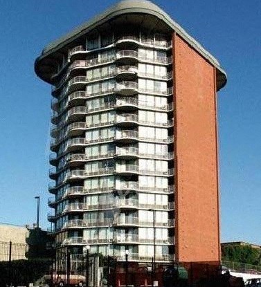 A tall building with a curved top and a red section on the side.