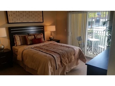 a bedroom with a bed and a sliding glass door  at Tesoro Senior Apartments, Porter Ranch, California - Photo Gallery 5