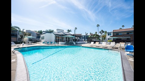 A large swimming pool with a blue tiled edge and white lounge chairs on the side.