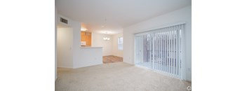 A spacious living room with a white carpet and a sliding glass door.
