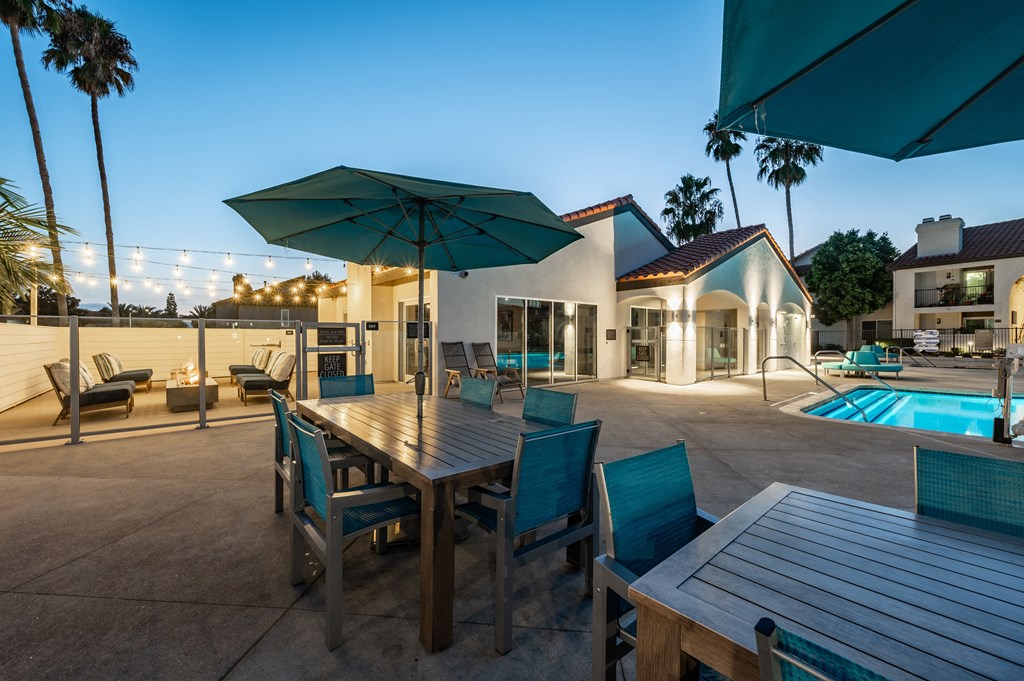 a dining table with chairs and umbrellas next to a pool  at Laguna Gardens Apts., California, 92677