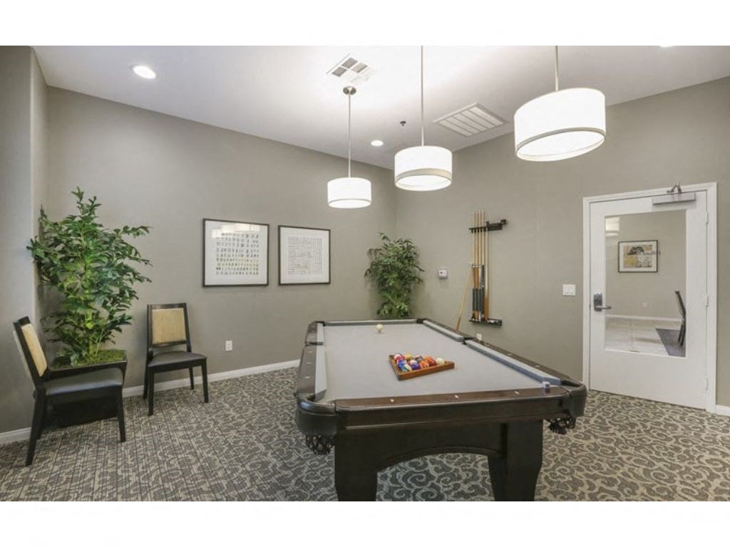 a game room with a pool table and two chairs  at Tesoro Senior Apartments, Porter Ranch, CA