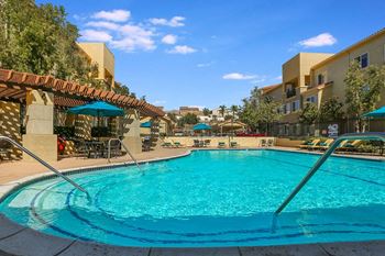 a swimming pool with umbrellas and buildings in the background  at Tesoro Senior Apartments, Porter Ranch, CA