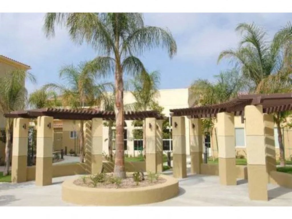 a courtyard with palm trees and a building in the background  at Tesoro Senior Apartments, Porter Ranch, California