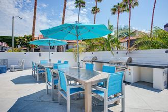 a patio with a grill and tables with blue chairs and umbrellas  at Laguna Gardens Apts., Laguna Niguel