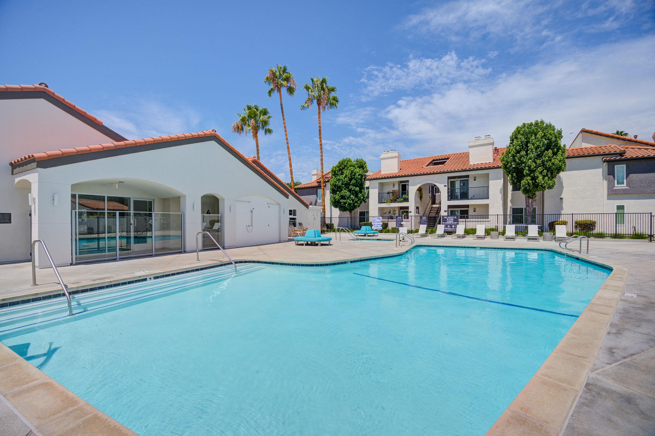 a large swimming pool with lounge chairs and palm trees in the background  at Laguna Gardens Apts., Laguna Niguel, California