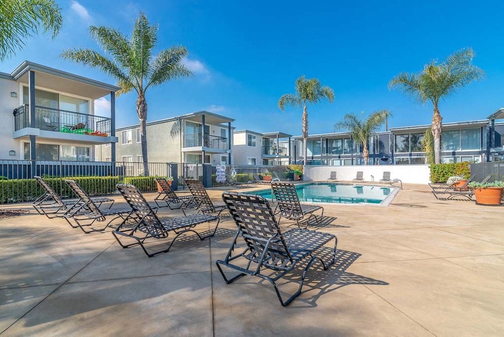 a swimming pool with chaise lounge chairs and palm trees in the background at  Park Avenue Apartments, California,90815
