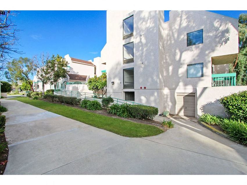 a white apartment building with a sidewalk in front of it a white apartment building with a sidewalk in front of it at Harvard Manor, Irvine, 92612 - Photo Gallery
