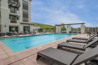 a swimming pool with chaise lounge chairs and a building in the background a swimming pool with chaise lounge chairs and a building in the background at Deer Creek Apartments, San Ramon, CA