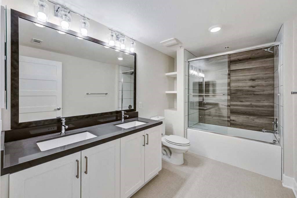 a bathroom with a toilet sink mirror and shower at The Vineyards Apartments, Porter Ranch, California