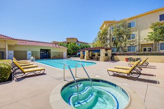 a swimming pool with a hot tub and lounge chairs with a hotel in the background  at Tesoro Senior Apartments, Porter Ranch, California