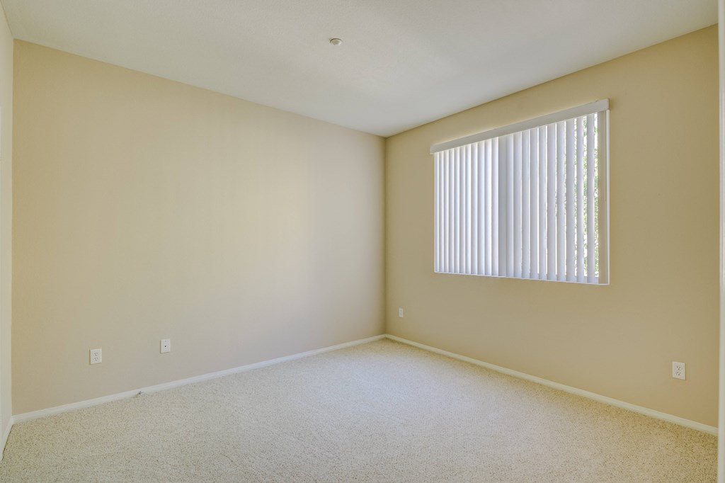 a bedroom with a large window and beige walls  at Tesoro Senior Apartments, California, 91326