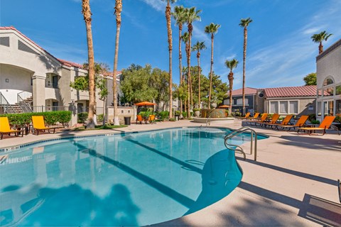 a swimming pool with yellow chaise lounge chairs and palm trees in the background at Rancho Serene, Las Vegas, NV