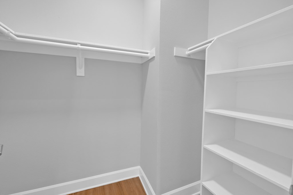 an empty closet with white shelves and a wood floor
