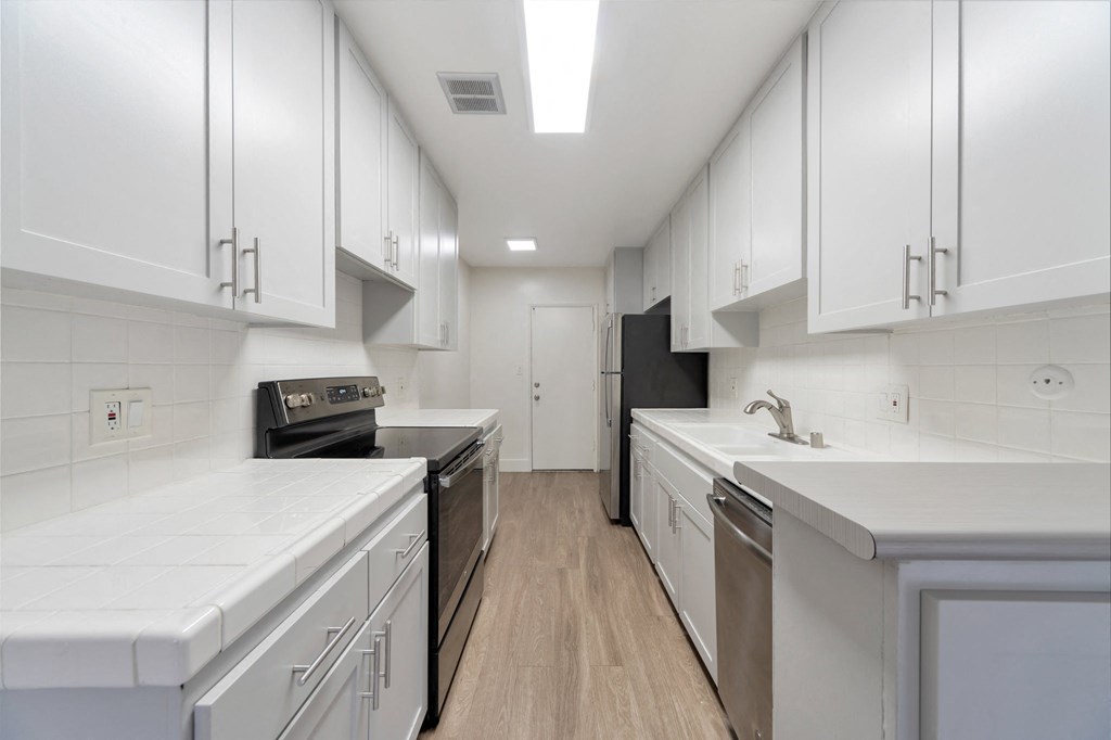 a kitchen with white cabinets and stainless steel appliances and white counter tops at The Mark Culver City, Culver City