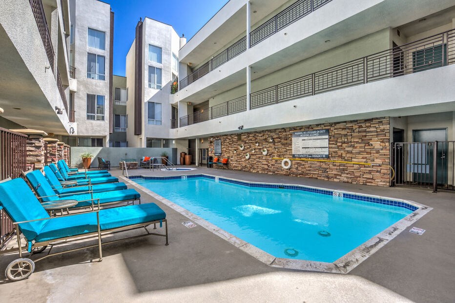 the pool is between two buildings and has blue lounge chairs