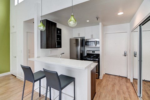 a kitchen with white cabinets and a white counter top with three stools in front of it  at El Greco Lofts, Los Angeles, CA, 90024