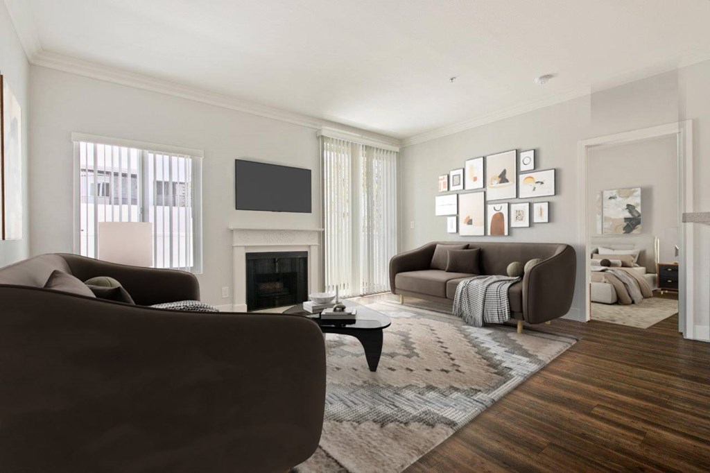 A living room with a brown couch, a fireplace, and a TV on the wall at The Plaza Apartments, Los Angeles