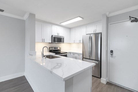 A modern kitchen with white countertops and stainless steel appliances.
