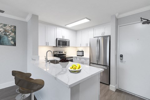 a kitchen with white cabinetry and a large white island with a bowl of fruit on it at Nobel Court, San Diego, 92122