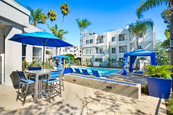 a swimming pool with tables and chairs and umbrellas in front of a building at Nobel Court, San Diego, CA