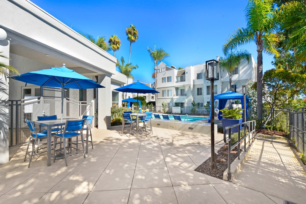 a patio with blue chairs and umbrellas and a swimming pool at Nobel Court, San Diego, CA