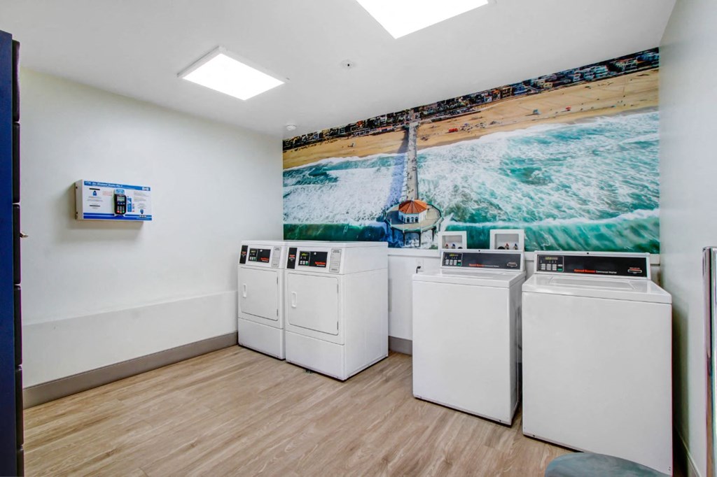 a laundry room with four washers and a painting of a beach on the wall at The Kenmore Los Feliz, Los Angeles, CA