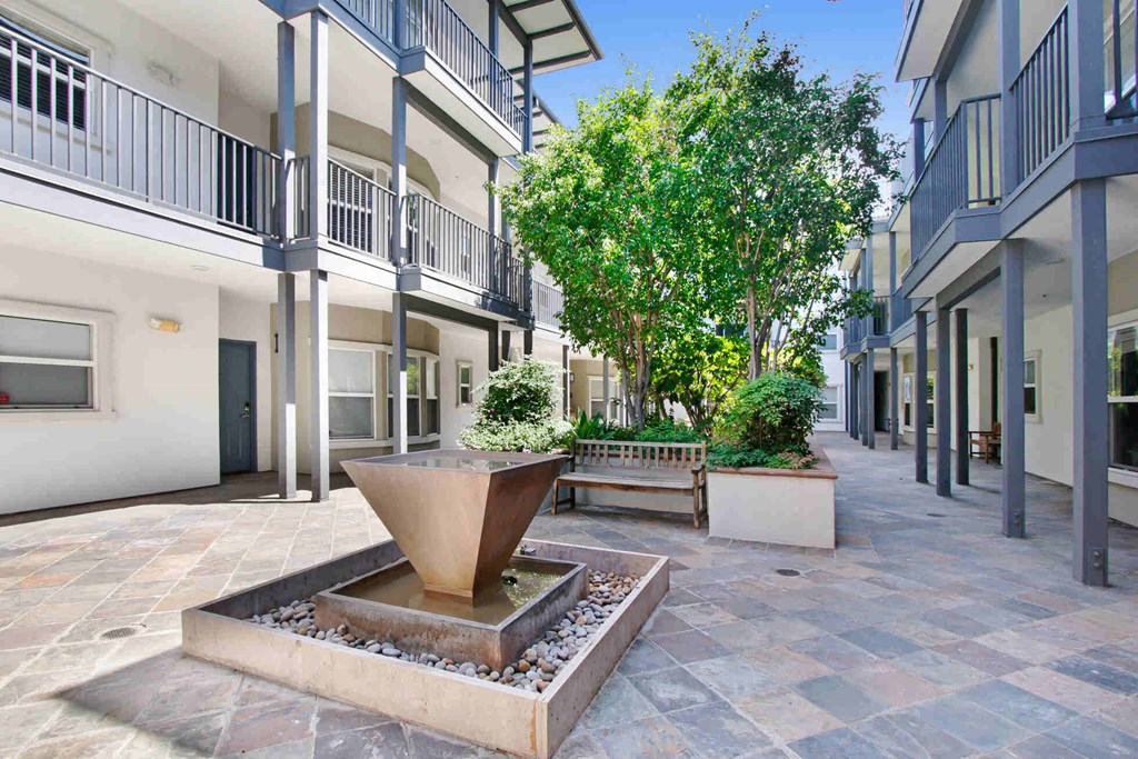 a fountain sits in the middle of a courtyard with trees and benches at Toluca Court, Toluca Lake