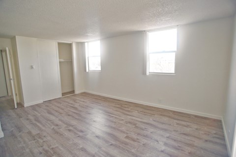 A room with light vinyl flooring and two windows.