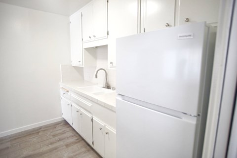 A white kitchen with a sink and a refrigerator.