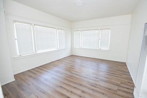 A room with wooden flooring and two windows with blinds.