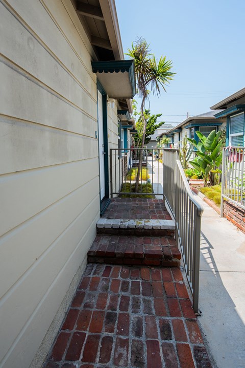 A small brick walkway leads to a door on a tan building.