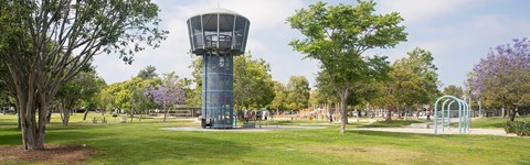 A large water tower in a park with trees and a playground.