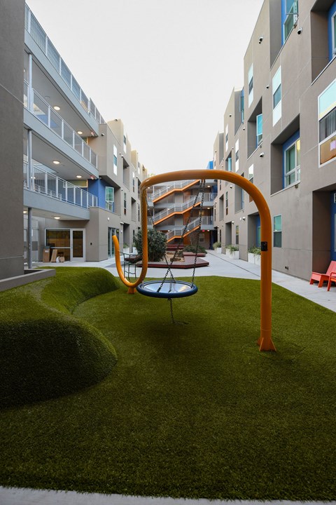 A playground with a swing set in the middle of a grassy area in front of apartment buildings.