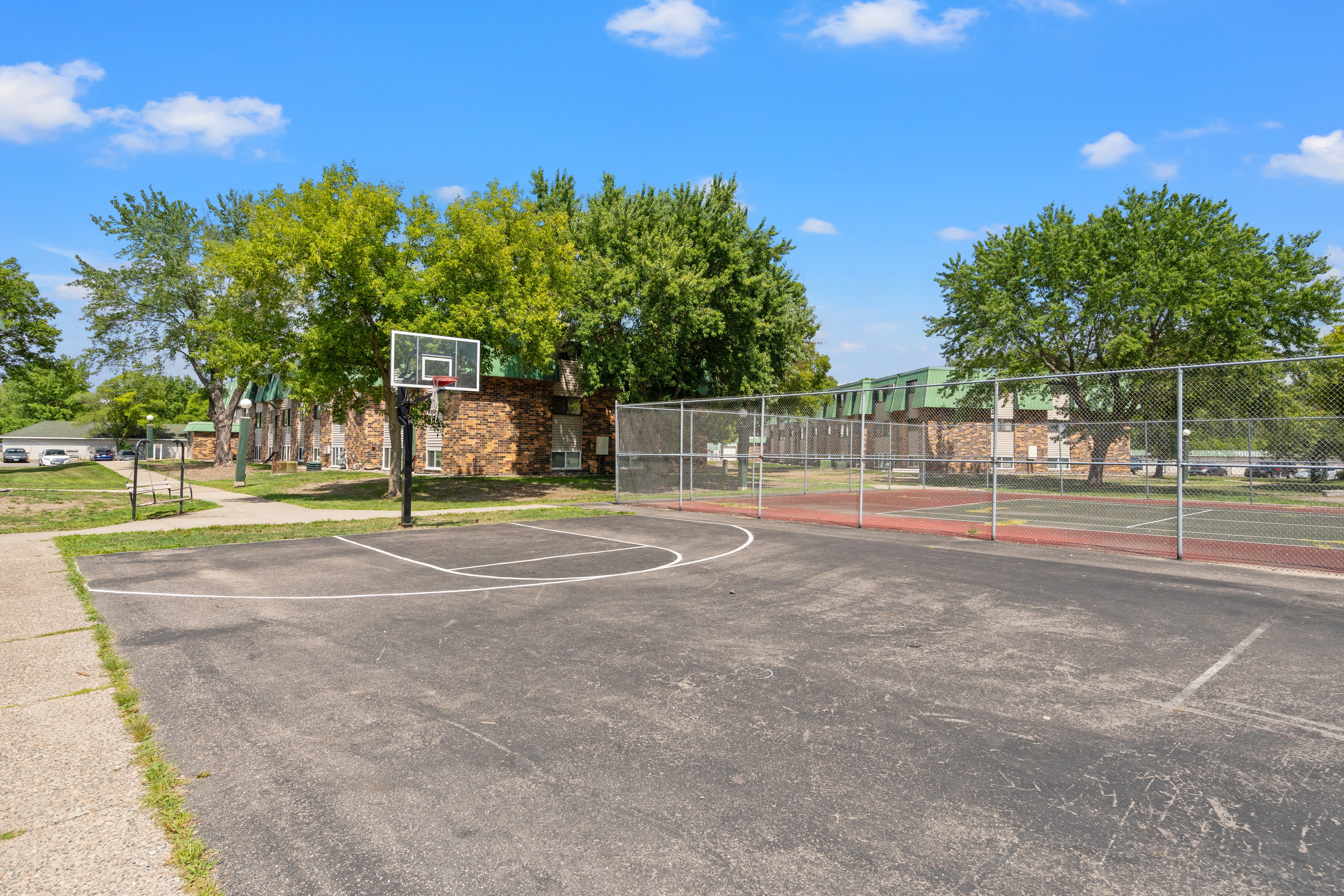 a basketball court in a park with trees and a building in the background
