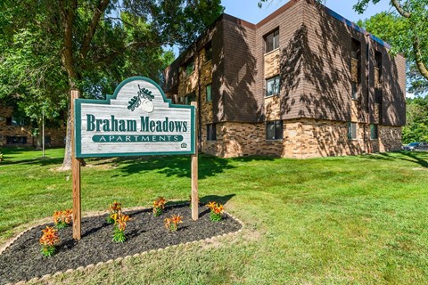 A sign for Braham Meadows Apartments stands in front of a brick building.