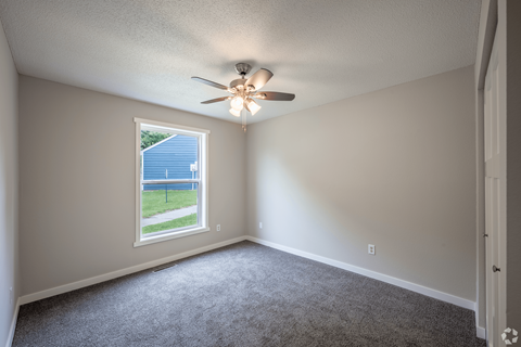 A room with a ceiling fan and a window overlooking a blue fence.