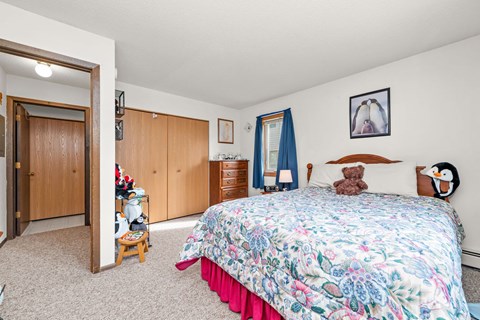 A bedroom with a floral bedspread and a teddy bear on the bed.