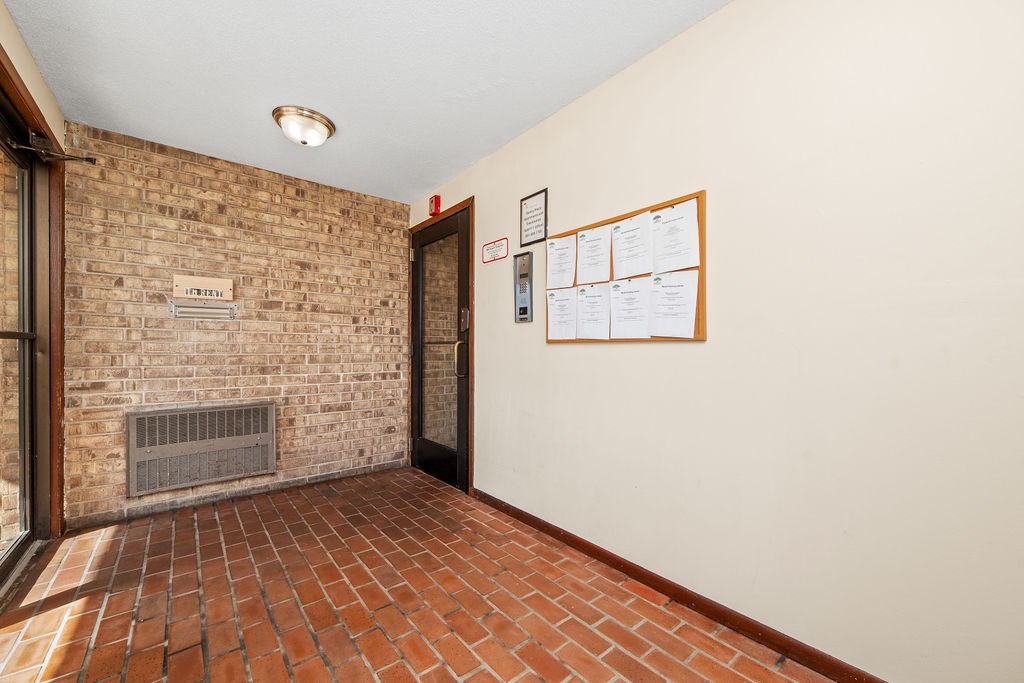 A hallway with a brick wall and a bulletin board on the wall.