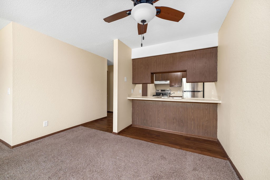 A room with a ceiling fan and a small kitchenette.