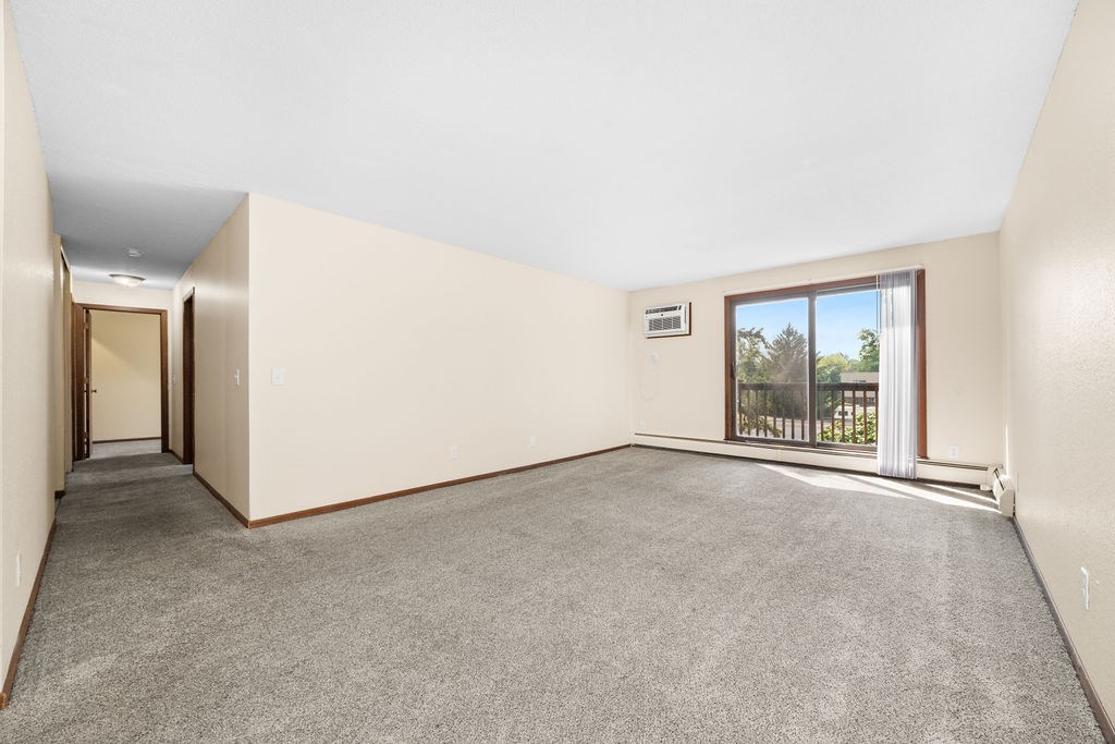 A room with a grey carpet and a window overlooking a balcony.
