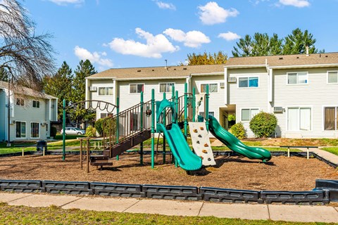 A playground with a green slide and a brown swing set.