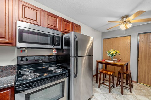 A kitchen with a stove, microwave, refrigerator, and a table with chairs.