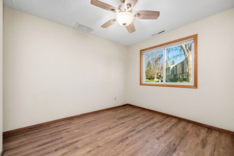 A room with a ceiling fan and a window showing a tree and a building outside.