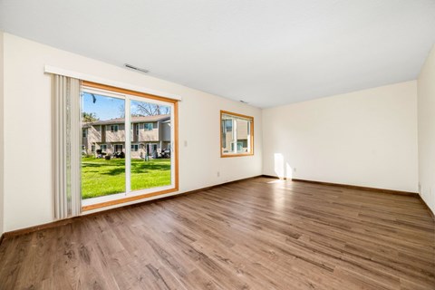 A room with wooden floors and a large window showing a view of a house.