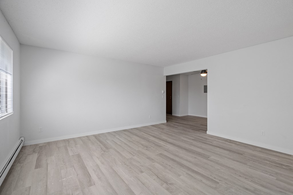 the living room and dining room of an apartment with white walls and wood flooring